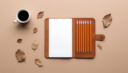 Open notebook with blank pages, pencils and coffee cup surrounded by dry autumn leaves on a beige background, inspiring creativity and writing