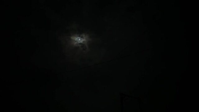 Mesmerizing view of the moon playing hide and seek behind drifting clouds on a dark, tranquil night.