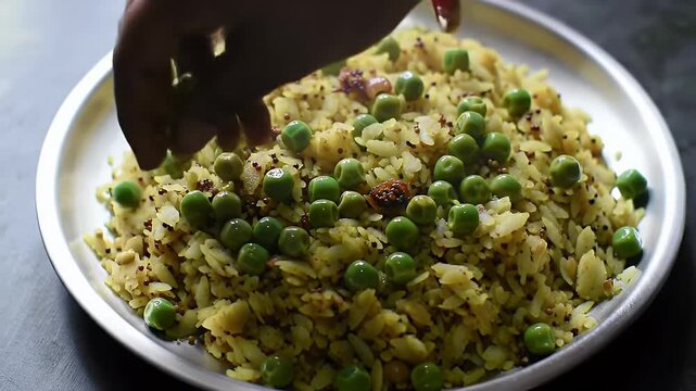 Vibrant Indian Poha with Green Peas and Mustard Seeds Traditional Vegetarian Dish on a Silver Plate a Hand Adds Fresh Peas Perfect for Healthy Eating Concepts and Indian Cuisine Close Up Video