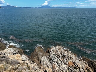 Rocky coastline under a clear blue sky, with rugged stones and boulders along the shore. Gentle...