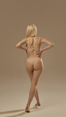 Blonde woman in beige lingerie back view with hands on waist walking with elegance. Concept of...