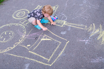 Little child creating colorful chalk art on pavement while sitting outside on a sunny day