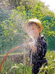 Child plays joyfully in garden while watering plants on a sunny day with a hose