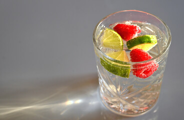 A close-up of a refreshing summer drink in a crystal glass, filled with sparkling water, fresh lime...
