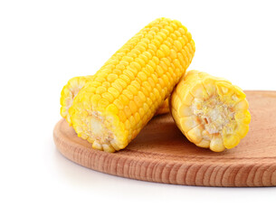 Boiled sweet corn cobs on a round wooden board.