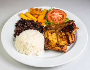 Grilled chicken breast with rice, black beans, and fresh vegetables on a white plate. Generative AI