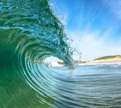 View of a translucent wave curling with explosive energy, contrasting shades of turquoise and blue against the distant shore, Redhead Beach, Newcastle, Australia.