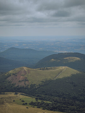 View of a volcanic crater nestled amidst lush green hills under a cloudy sky, creating a serene yet dramatic landscape, Chaine des Puys, Auvergne-Rh&Atilde;&acute;ne-Alpes, France.