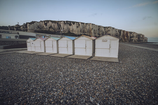 View of quaint white beach huts stand in a neat row on a pebble beach under the imposing chalk cliffs, a serene coastal scene, Le Tr&Atilde;&copy;port, Normandy, France.