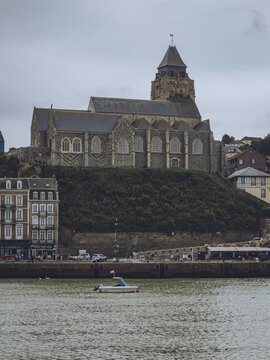 View of a boat sailing on the water with the old stone church standing tall on the hill behind the buildings, Le Tr&Atilde;&copy;port, Normandy, France.