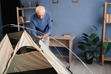 A pensioner setting up a camping tent prepares for a hike and checks equipment at home