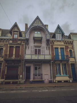View of a row of colorful, vintage townhouses stand beneath a cloudy sky, showcasing unique architectural details and vibrant facades, Mers-les-Bains, Hauts-de-France, France.