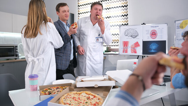 A group of people are eating pizza in the clinic's medical laboratory. Several doctors are enjoying a delicious hot pizza on their lunch break. Coffee break at work