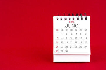 White desk calendar for June 2026 on red color background.