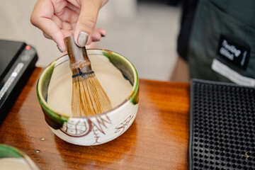 Hand using bamboo whisk to prepare matcha tea in ceramic bowl reflects traditional Japanese style...
