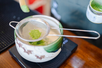 Matcha powder being sifted into traditional ceramic bowl reflecting japanese culture and style with...