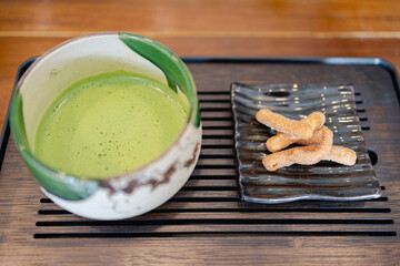 Traditional Japanese tea ceremony with bowl of frothy green matcha and sweet snacks on wooden tray...