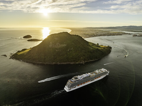 Mount Maunganui, New Zealand - 10 January 2024: Aerial view of the majestic Mauao, its verdant slopes contrasting against the deep blue sea, with a cruise ship sailing towards the horizon.