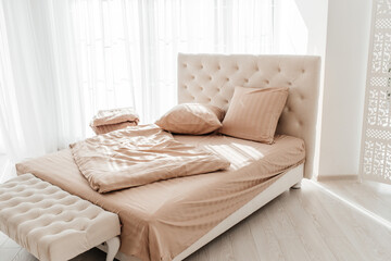 Cozy beige bed with soft pillows and blanket in bright sunlight