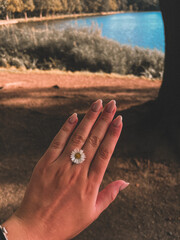 Hand wearing a flower-shaped ring in natural sunlight.