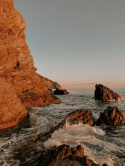 Red coastal cliffs with waves crashing at sunset.