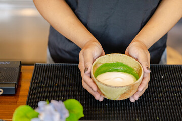 Traditional ceramic bowl with matcha tea held by person hands on black mat reflecting japanese style culture and calm atmosphere