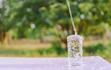 Refreshing pure water splashing out of a glass on a bright outdoor background, symbolizing...