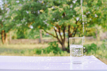 Refreshing pure water splashing out of a glass on a bright outdoor background, symbolizing...