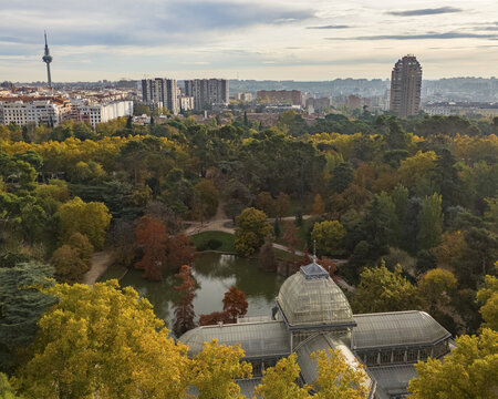 Aerial view of parque el retiro with palacio de cristal, trees, and pond surrounded by urban landscape, Retiro, Madrid, Spain.