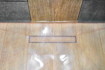 Wooden shower floor with water pooling around drain, suggesting clog. Minimalist design and neutral...