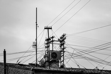 Black and white rooftop photo of intersecting power lines and antennas, capturing urban tension and...