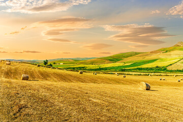 Scenic view at picturesque burning sunset in a green shiny field with hay stacks, bright cloudy sky...