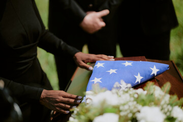 Black woman placing hands on casket draped with folded American flag during funeral ceremony, two...