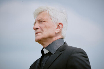 Senior Caucasian man wearing clerical collar standing outdoors gazing into distance, officiating...