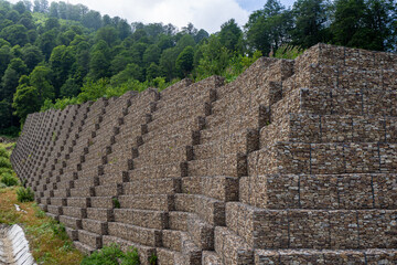 Gabion wall terraces securing steep alpine hillside. Reinforced stone retaining wall on mountain...