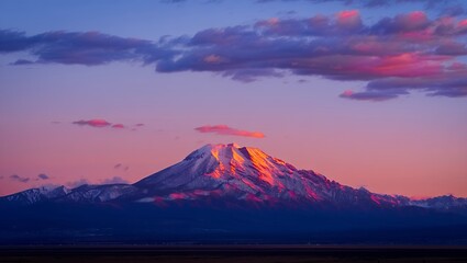 A majestic, snow-covered mountain peak glows with pink alpenglow during a vibrant sunset.