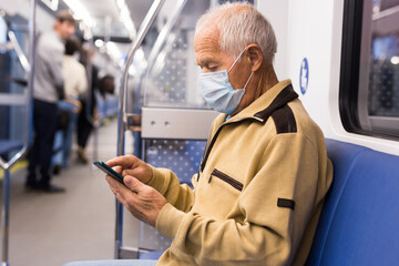 Elderly man in mask in subway car with smartphone