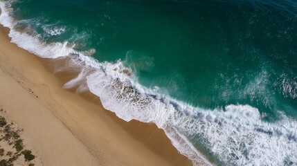 Highangle view of gentle ocean waves crashing onto sandy shoreline with sunlight reflections and organic foam patterns, lush background, and tranquil coastal ambiance