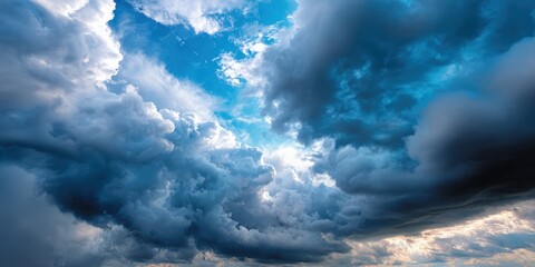 Dramatic sky with dark voluminous storm clouds contrasting with bright sunlit patches and clear blue sky