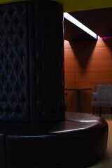  Contemporary lounge interior featuring a circular leather seating area with tufted details. The modern design is complemented by a cozy corner with chairs and a table set against wooden paneling.