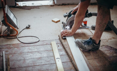A worker is sawing a board with an electric saw.