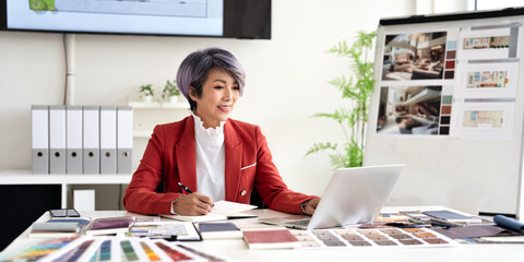 Interior designer working on her project  in studio office holding pen taking notes in a notepad .
