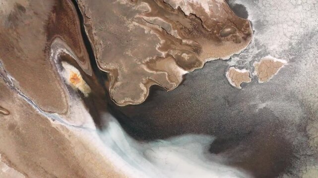 Aerial view of a dry, cracked, salt-crusted desert landscape with gray water of Lake Assal