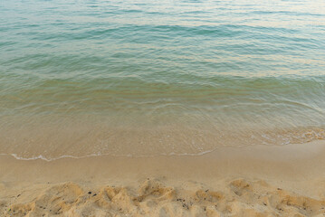 Gentle sea waves reaching sandy beach under warm evening light