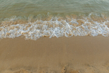 Small sea waves breaking on sandy beach in soft sunset light