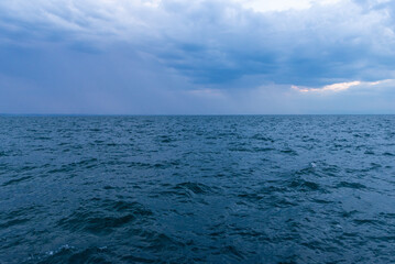 Obraz premium Blue ocean under cloudy sky with distant rain on the horizon, perfect for weather, travel, or adventure backgrounds