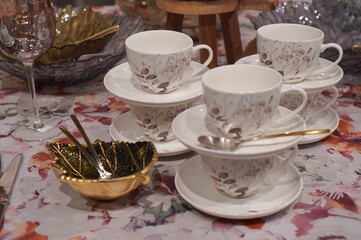  Charming tea set with floral-patterned cups and saucers, elegantly arranged on a floral-printed tablecloth. Delicate gold and silver accents add a touch of sophistication to the setting.