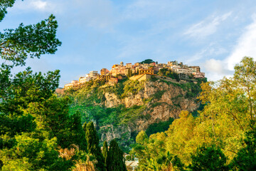 beautiful highland landscape of old town on a top of amazing mountain with green slopes and trees on foreground and amazing blue cloudy sky on background