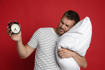 Man with pillow and alarm clock suffering from hangover on red background