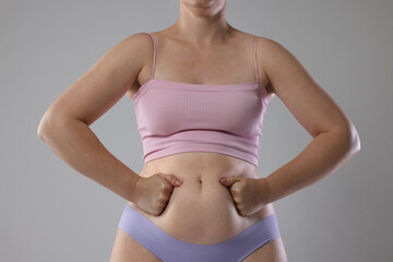 Liposuction. Woman in underwear touching her belly on grey background, closeup